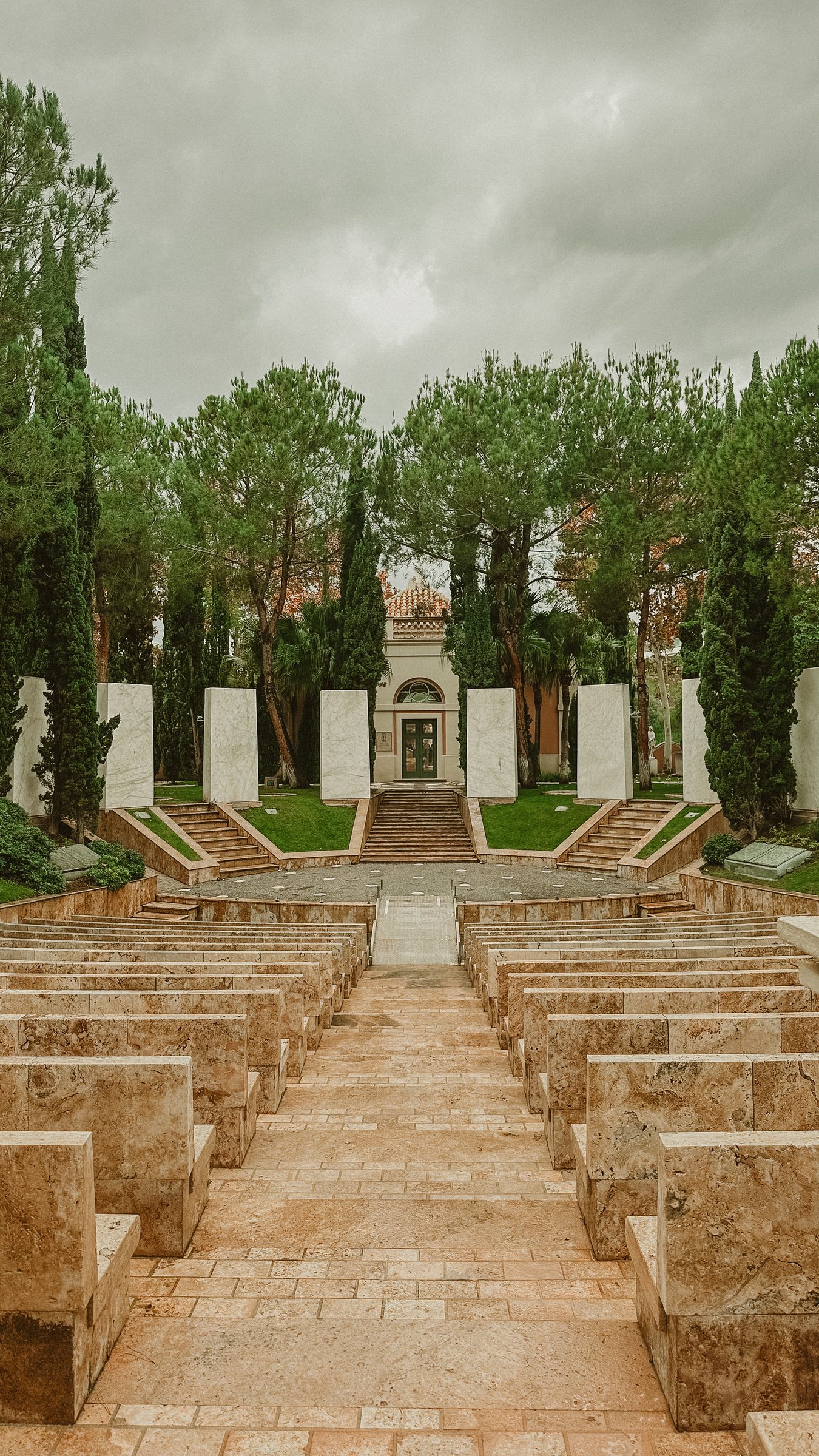 A wide stone staircase flanked by cypress trees leading up to the colonnaded entrance of the palace