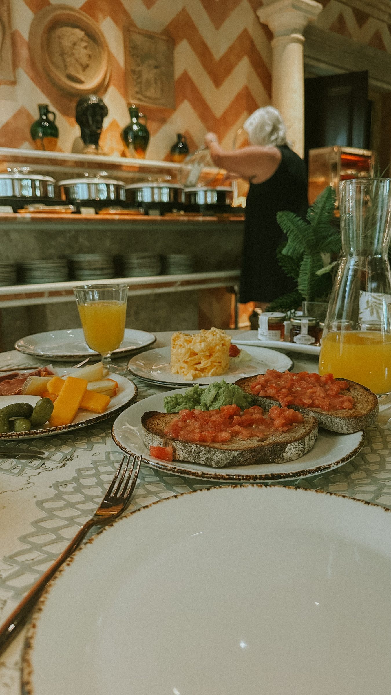 A breakfast table with tomato toast, fruit, orange juice and a buffet behind