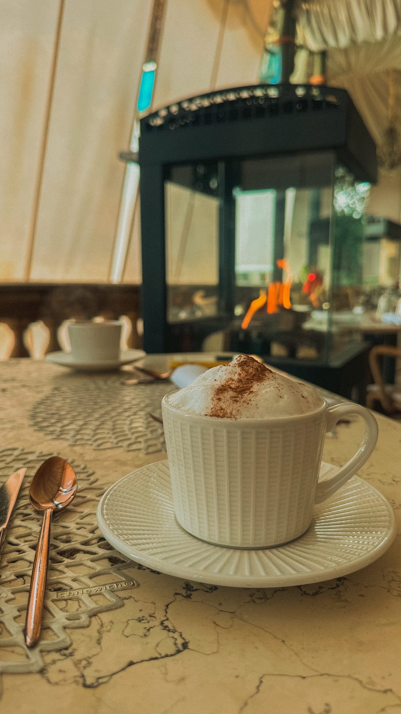 A cappuccino in a fluted white cup on a marble table beside a black lantern