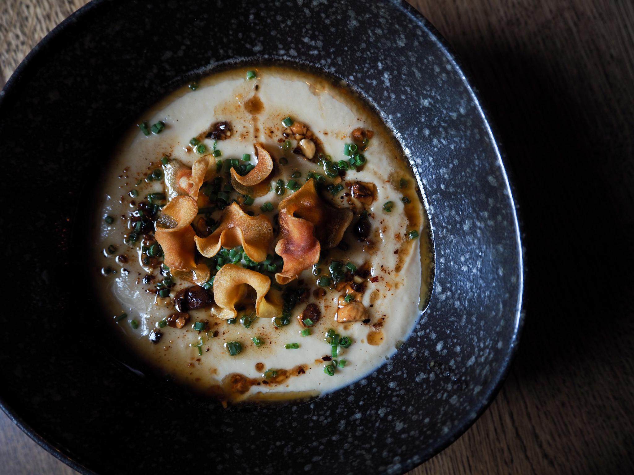 A pale puree in a dark speckled bowl topped with crisped root vegetables and chives