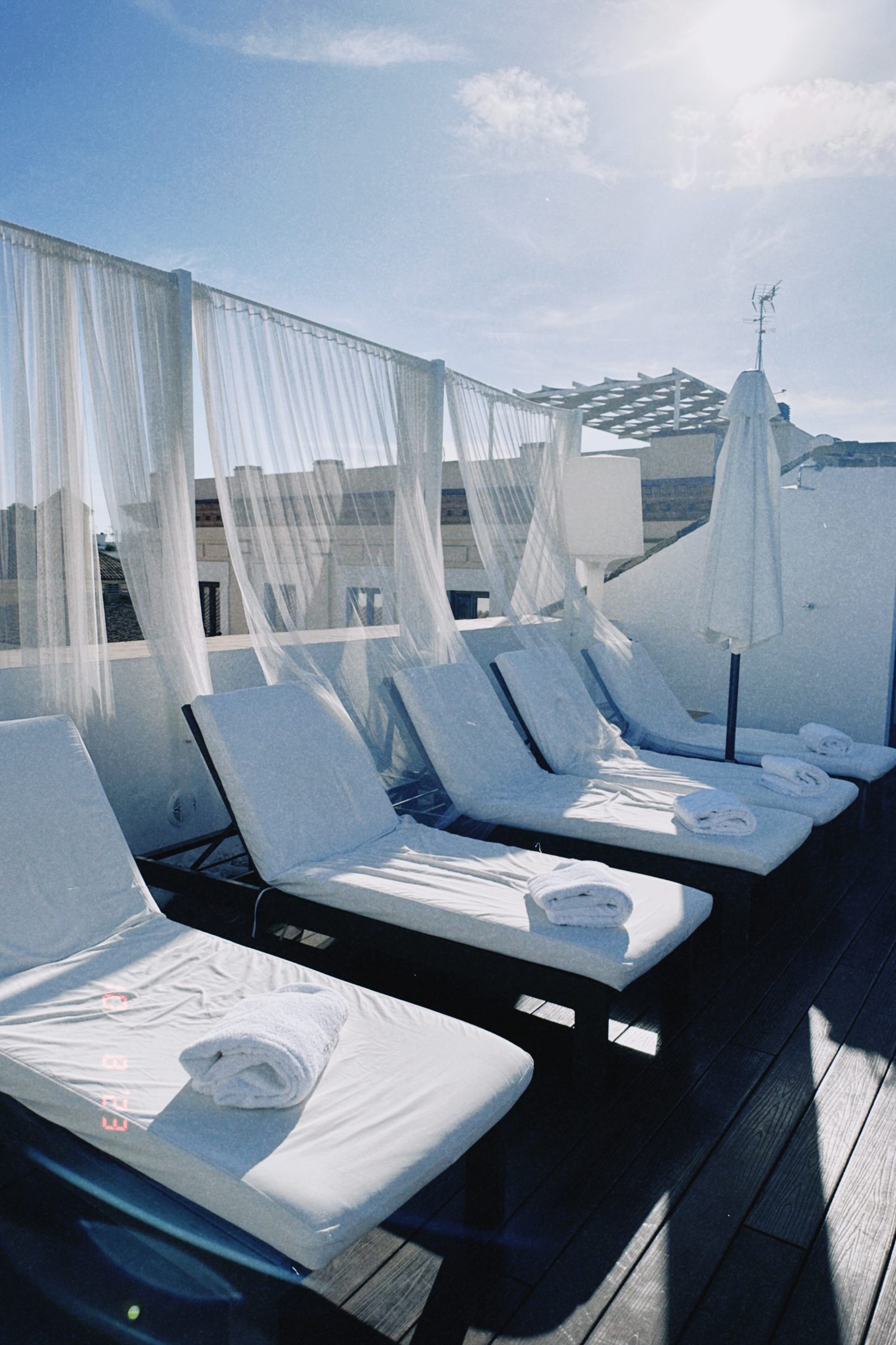 Loungers and white voile curtains on a Seville rooftop under a blue sky