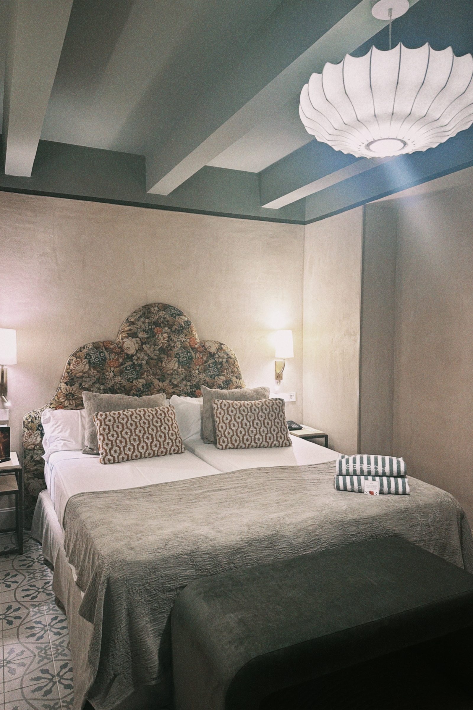 A hotel bedroom with painted beams, a floral headboard and patterned cement floor tiles