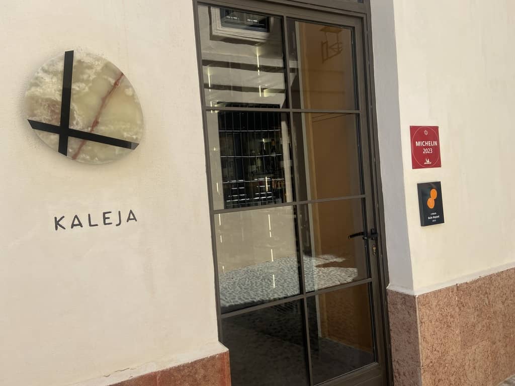 The doorway of Kaleja in Malaga, with its onyx disc sign and a Michelin plaque beside it