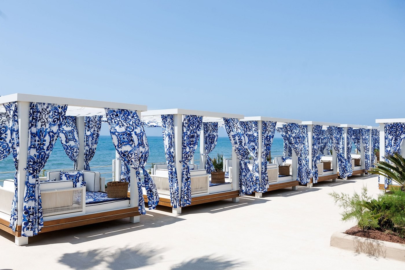 White cabanas draped in blue and white maiolica-print curtains facing the sea at La Cabane, Marbella