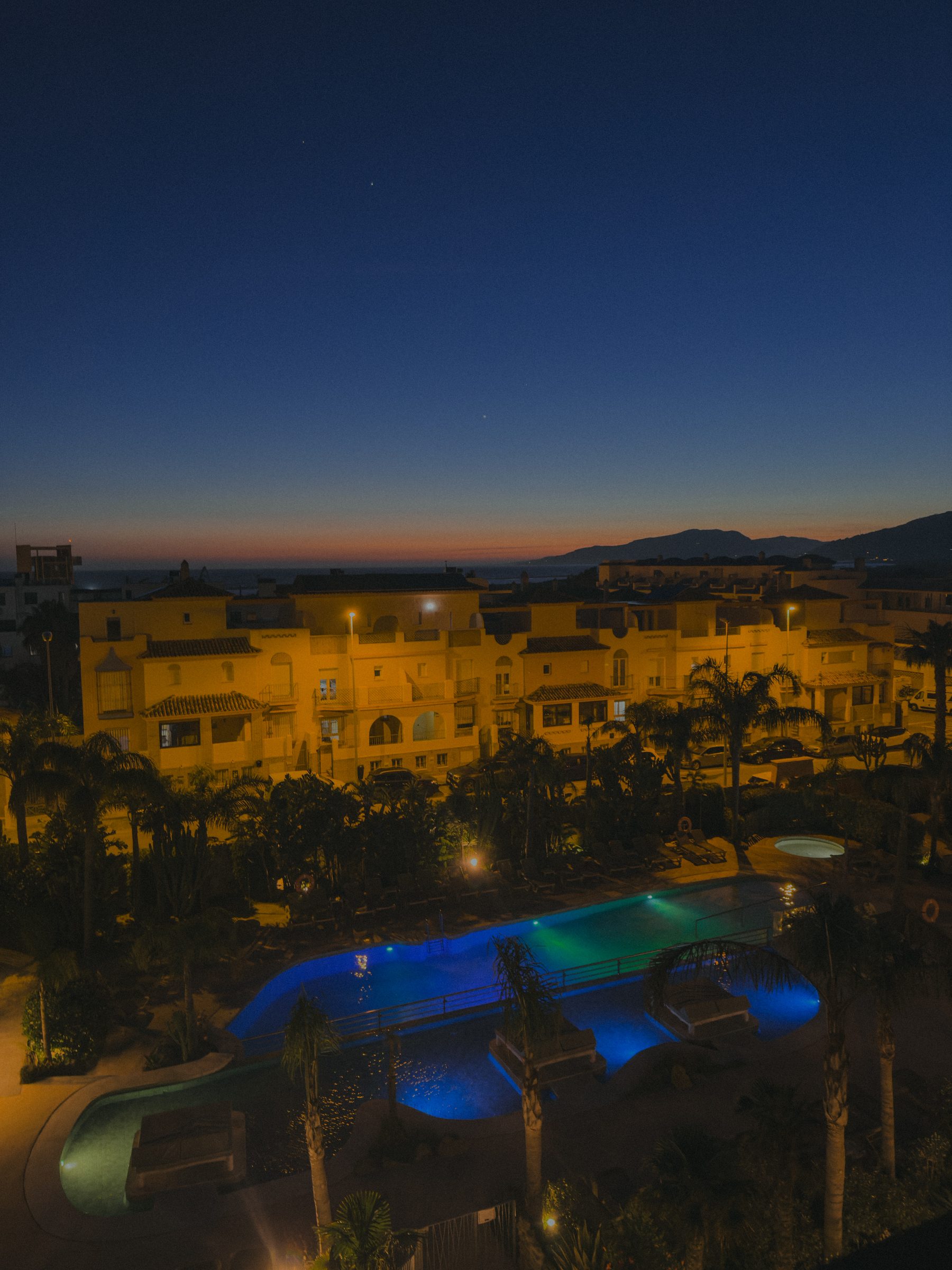 The hotel pool lit blue at dusk with the sunset over the mountains beyond