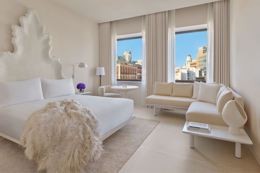 A pale room at The Madrid EDITION with a sculpted plaster headboard and windows over the rooftops