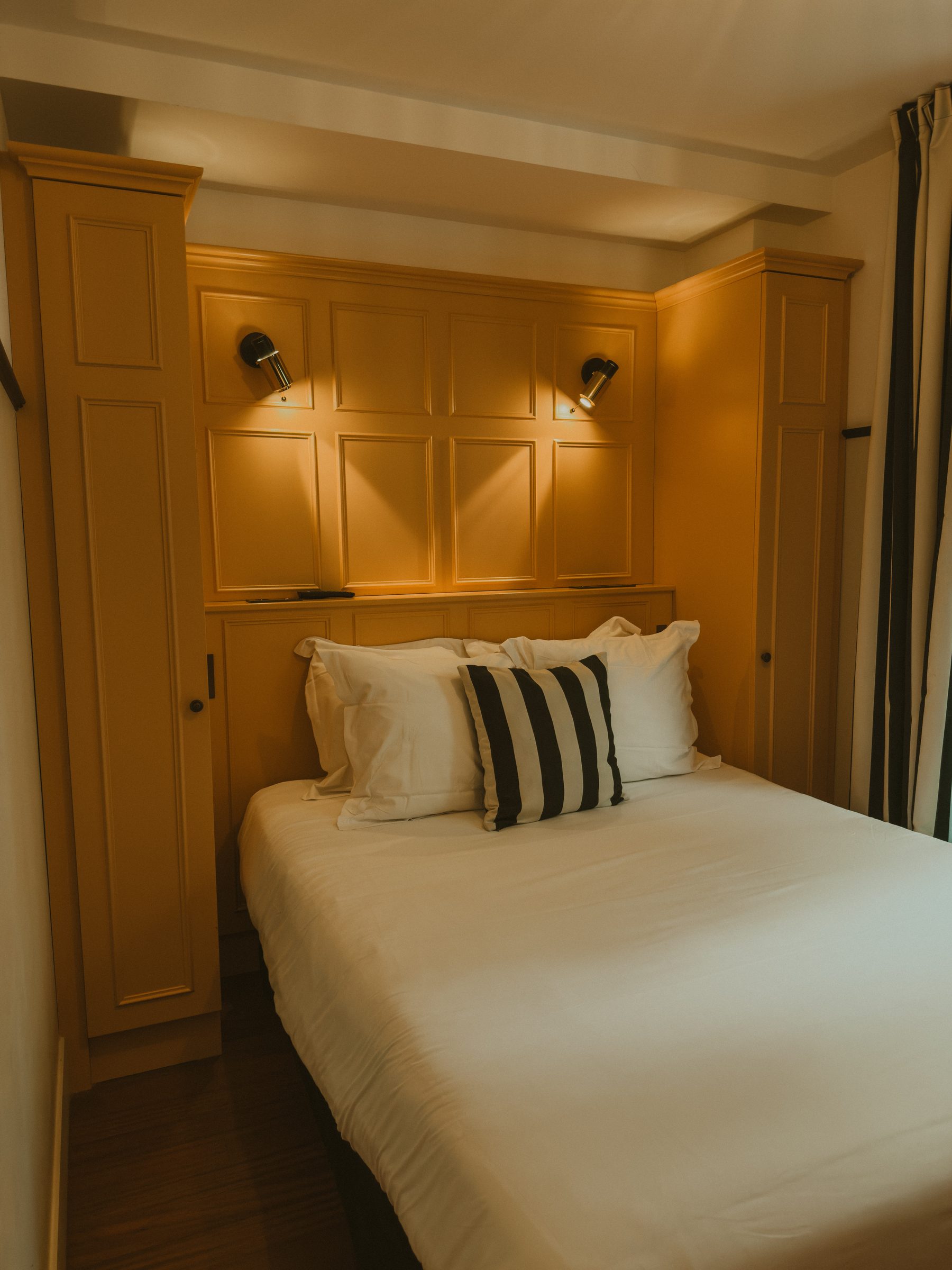 A bed set into ochre panelled joinery with built in wardrobes either side