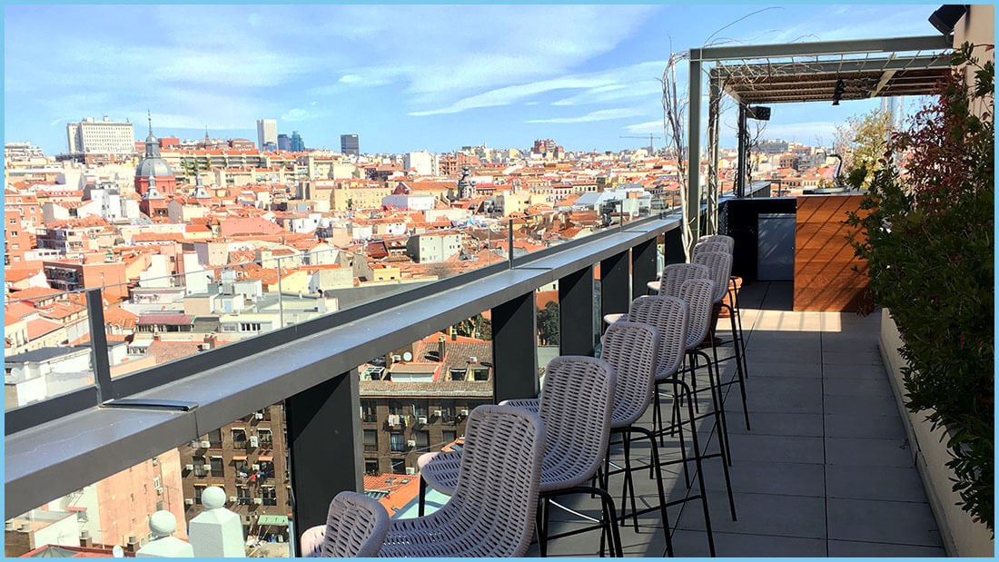 Wicker bar stools along the rail at the Nice To Meet You rooftop, looking over the tiled roofs of Madrid