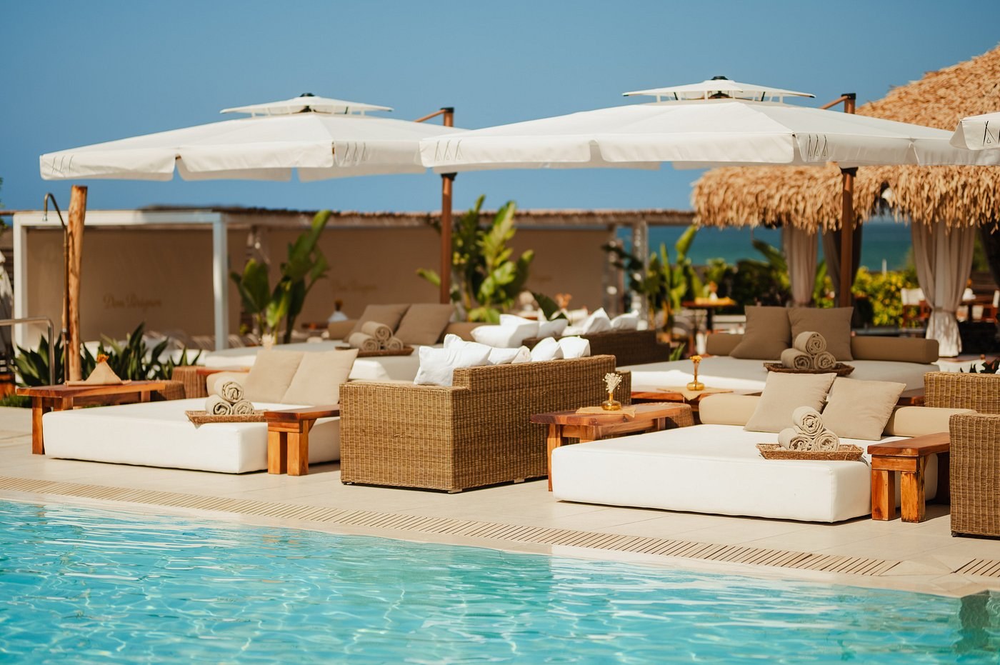 White daybeds and wicker furniture around the pool at Nikki Beach Marbella under thatched parasols